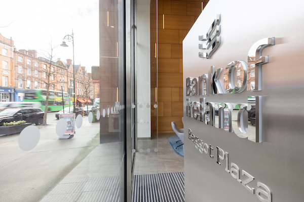 An image from inside Baggot Plaza looking sideways from the entrance. On the left is the window with a view of Baggot Street, and on the right is a view of the silver 'Bank of Ireland Baggot Plaza' sign.