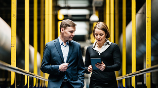 Two professional people walking and looking at a tablet.